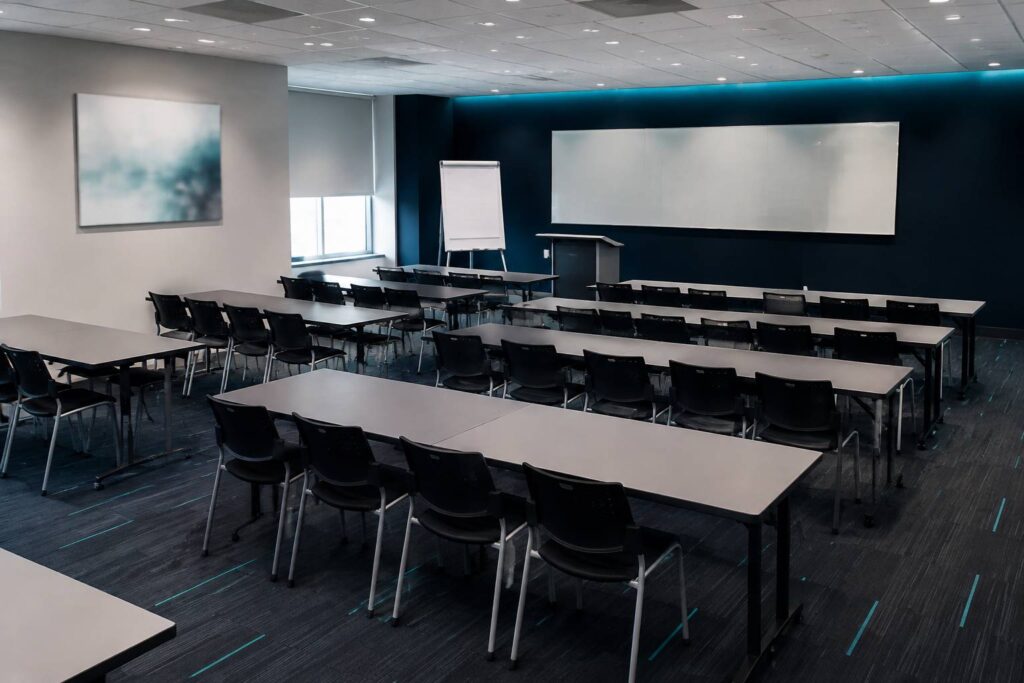 Grande salle d'association avec tables et chaises alignées et paperboard vierge, sans logo ni personne